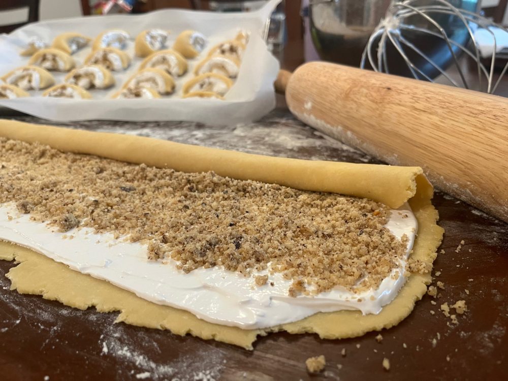 walnut cookies being rolled on table, rolling pin, and cookie sheet with cookies